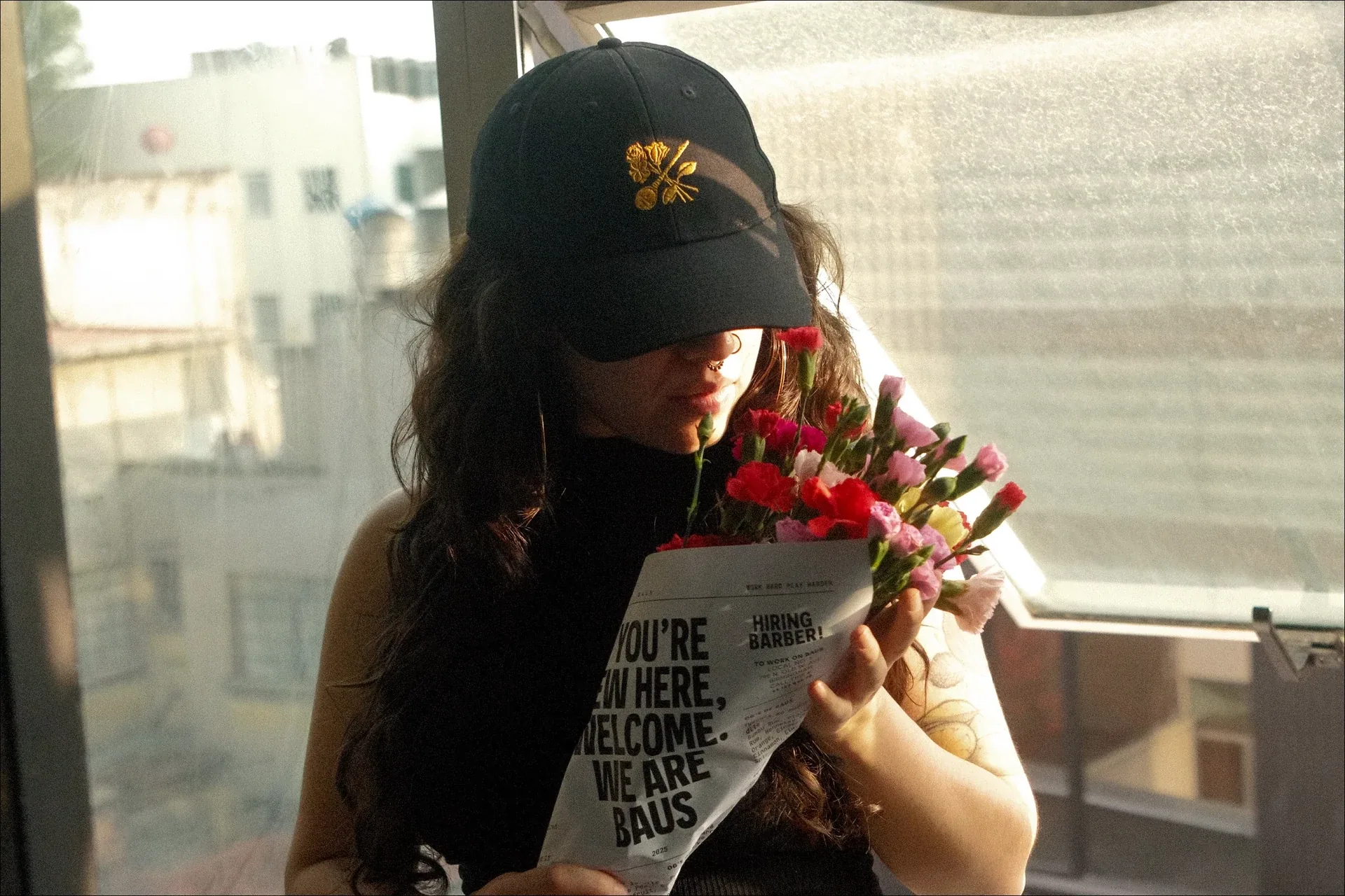 Woman wearing a Baus cap holding flowers wrapped in branded paper