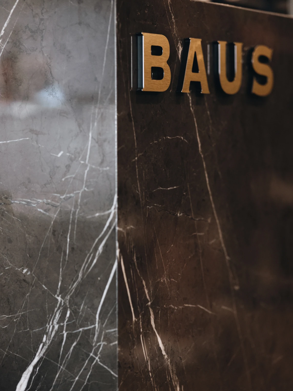 Baus logo in gold dimensional letters on a dark marble wall