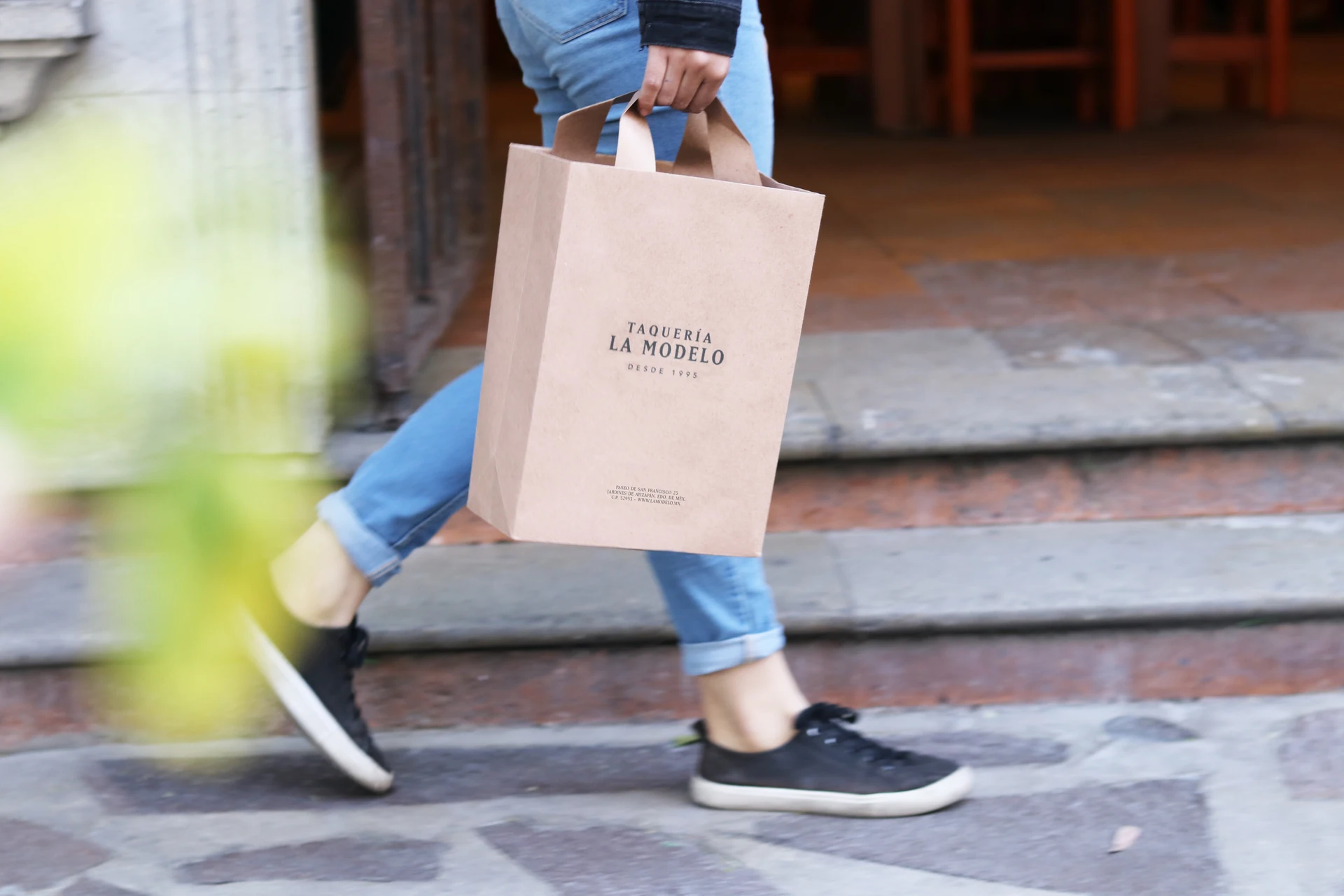 Person carrying a Taquería La Modelo shopping bag down the street