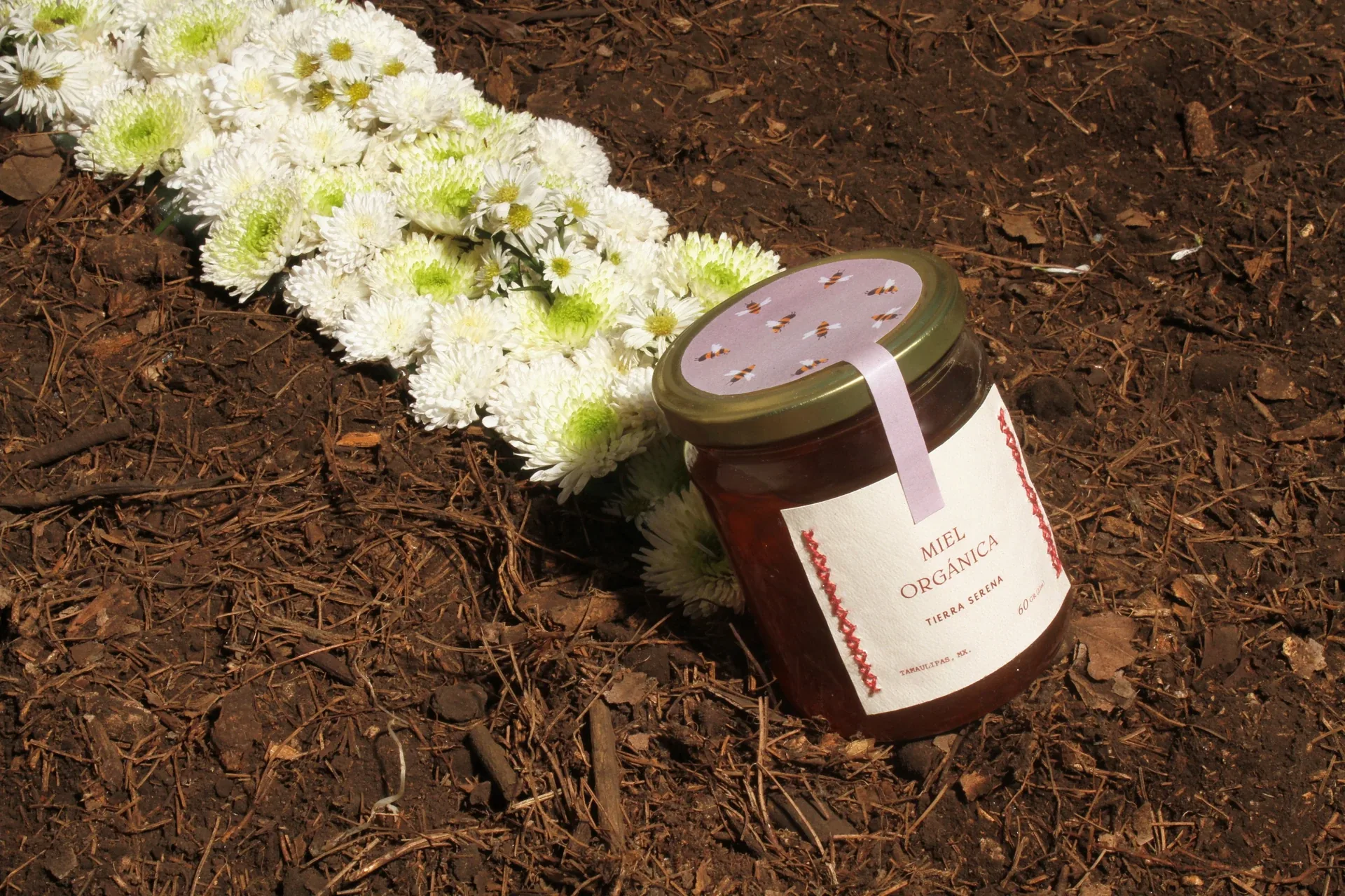 Tierra Serena organic honey jar on soil with white flowers