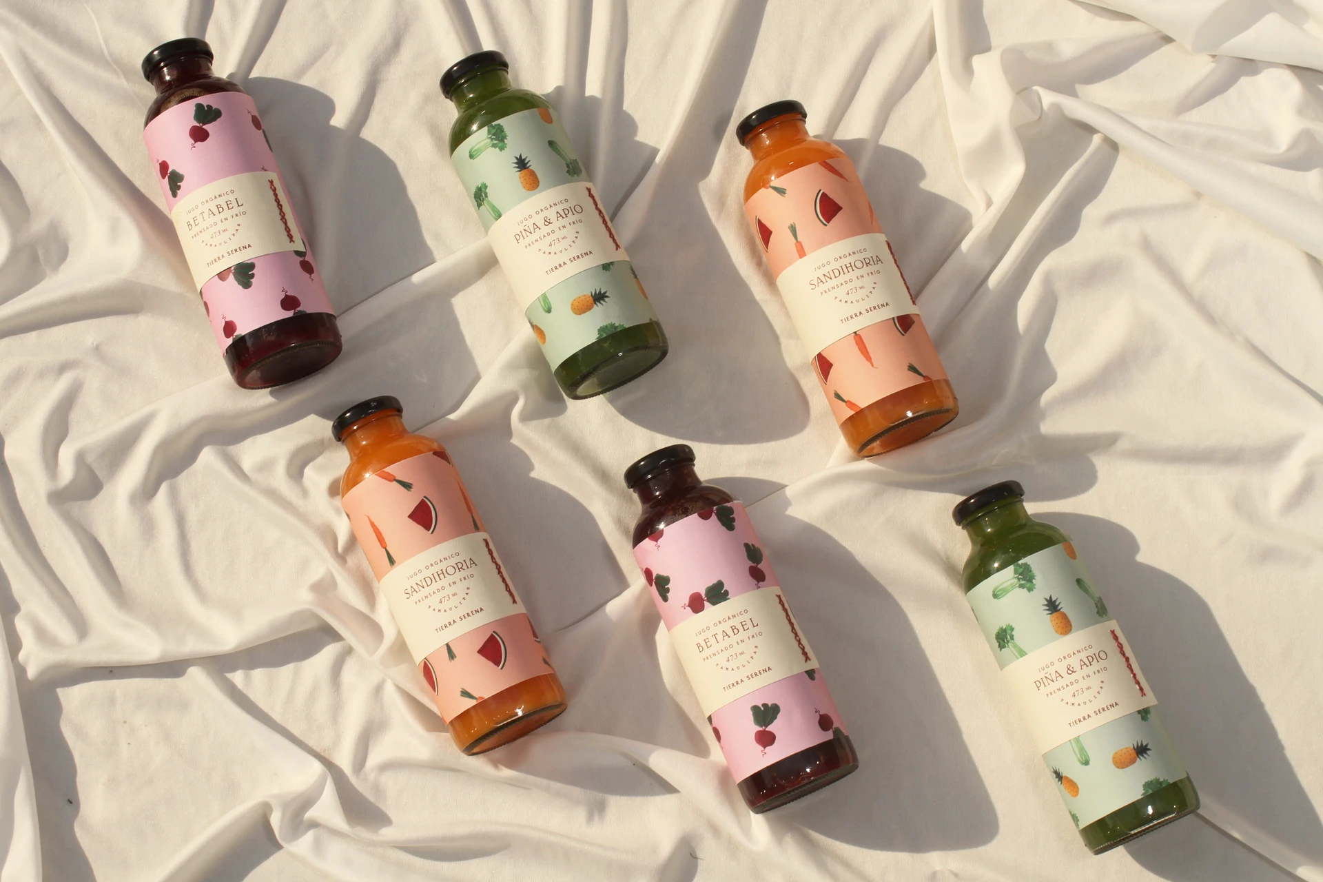 Six Tierra Serena juice bottles with illustrated labels on linen